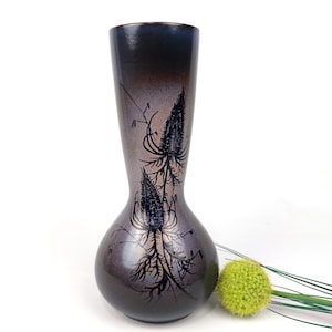 May include: A tall, decorative vase with a bulbous base and a slender neck. The vase is primarily gray with a gradient from dark blue to gray at the top. It features a black floral design. A green decorative ball and grass are next to the vase.