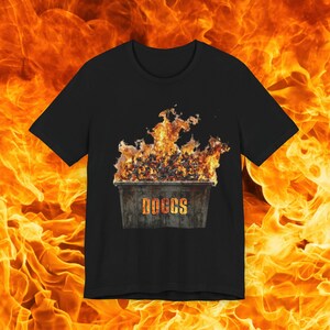 Op de afbeelding: Een zwart T-shirt met een afbeelding van een brandende vuilnisbak. De vuilnisbak is gelabeld met "DOCCS".