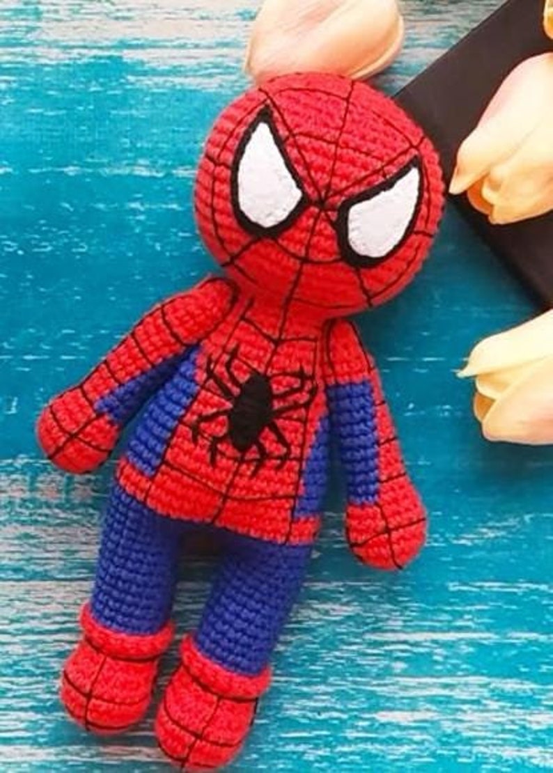 Puede incluir: Mu&ntilde;eco de Spider-Man hecho a mano con ganchillo. El mu&ntilde;eco presenta un disfraz rojo y azul con un emblema de ara&ntilde;a negra en el pecho. Los ojos son blancos y el mu&ntilde;eco est&aacute; hecho con hilo texturizado.