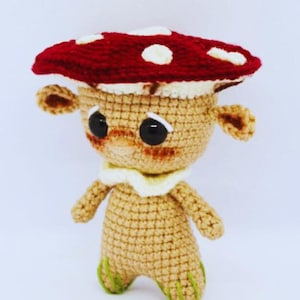 May include: A crocheted mushroom character with a red and white mushroom cap, brown eyes, and green feet.