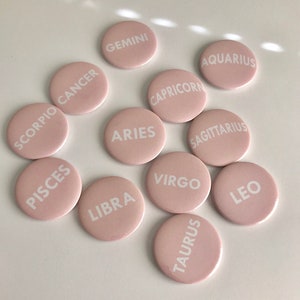 May include: Twelve pink round buttons with white text, each featuring a different zodiac sign: Aries, Taurus, Gemini, Cancer, Leo, Virgo, Libra, Scorpio, Sagittarius, Capricorn, Aquarius, and Pisces.