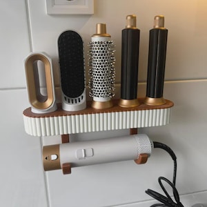 May include: A white and gold hair styling tool organiser with various attachments. The organiser has a shelf with a white and brown design, and a holder for a hairdryer. The attachments include brushes and styling tools.