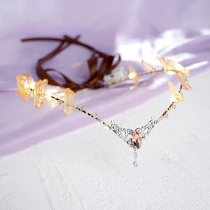 May include: A delicate silver headband with a crystal pendant and clear quartz crystals. The headband is adorned with small, clear beads and has a brown ribbon attached.