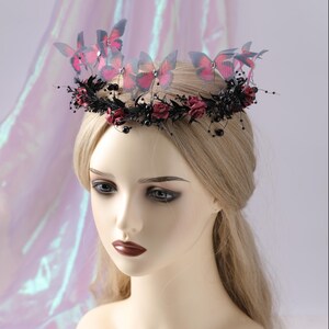 May include: A decorative headpiece featuring pink and gray butterfly accents. The crown is adorned with dark red roses, black berries, and delicate sprigs. The headpiece is designed for special occasions and events.