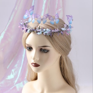 May include: A delicate floral crown featuring lavender and blue butterflies, small blue beads, and sprigs of greenery. The crown is set against a soft, iridescent background, creating a whimsical and ethereal aesthetic. Perfect for weddings, festivals, or themed events.