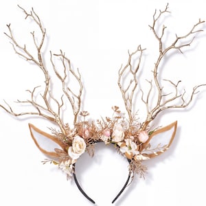 May include: A headband featuring two large, metallic gold-painted tree branches resembling antlers, accented with artificial cream and pale pink roses, gold-toned foliage, and two tan-colored felt ears extending from the sides of the band.