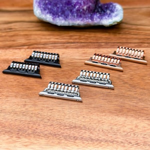 May include: Four Apple Watch band adapters in different finishes: black, silver, rose gold, and gold. The adapters are made of metal and have a sleek, modern design.