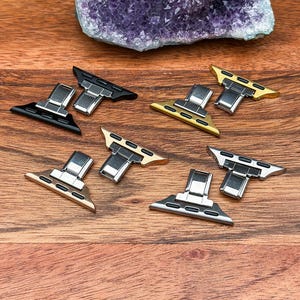 May include: Six different Apple Watch band adapters in various finishes, including black, silver, and gold. The adapters are designed to connect watch bands to the watch case.