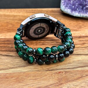 Puede incluir: Un reloj inteligente negro con una pulsera de cuentas verdes y negras. La pulsera est&aacute; hecha de cuentas de ojo de tigre y &oacute;nix.