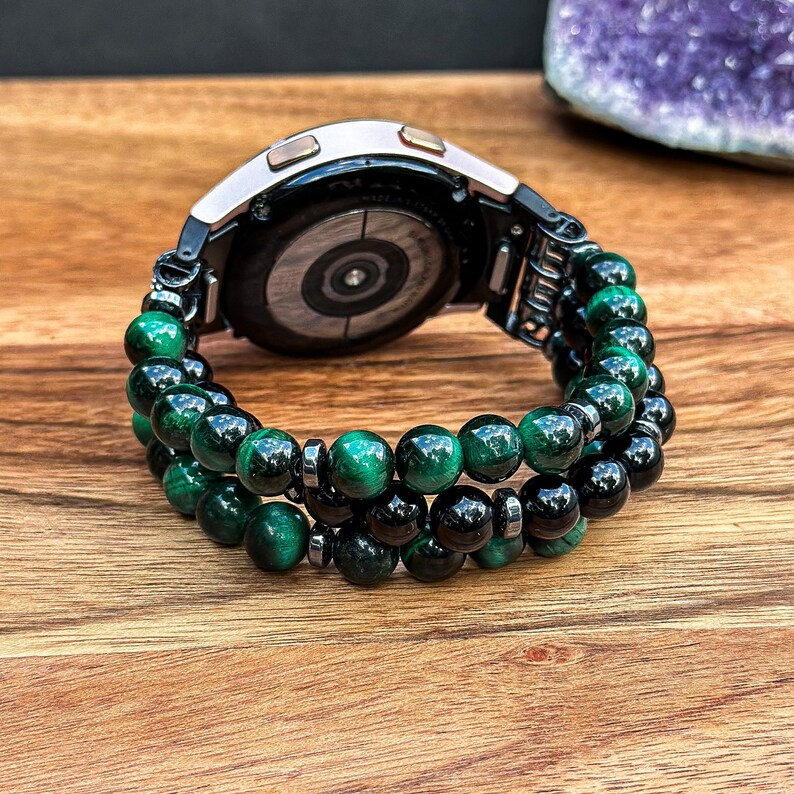 Puede incluir: Un reloj inteligente negro con una pulsera de cuentas verdes y negras. La pulsera est&aacute; hecha de cuentas de ojo de tigre y &oacute;nix.