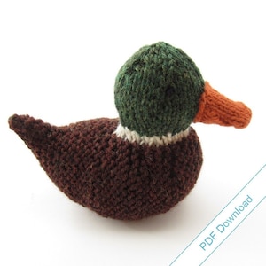 Puede incluir: Un juguete de peluche de pato silvestre tejido con lana marrón, verde, blanca y naranja. El pato tiene la cabeza verde, una franja blanca alrededor del cuello y un pico naranja.