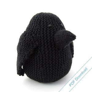 May include: Black knitted crow with black eyes. The crow is sitting on a white surface. PDF Download is written in the bottom right corner of the image.