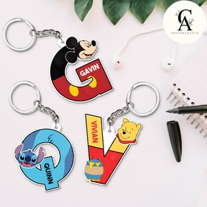 May include: Three character keychains with Disney character designs. The letter "G" features Mickey Mouse and the name "Gavin". The letter "Q" has Stitch and the name "Quinn". The letter "V" has Winnie the Pooh and the name "Vivian".