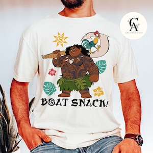 May include: White t-shirt with a cartoon image of a Polynesian man with tattoos holding a weapon. The man is wearing a green grass skirt. The text "Boat Snack!" is printed below the image.