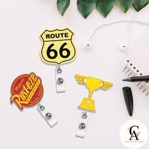 May include: Three themed retractable badge holders. One is yellow with a Route 66 design, another is red with "Rusteze" text, and the third is a gold trophy. Each has a white plastic clip and a retractable cord.