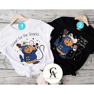 May include: Two white and black t-shirts with a cartoon mouse wearing a captain's hat and holding a cup of coffee. The white shirt says "Cruisin' for the Snacks" and the black shirt says "Cruisin' for the Snacks".