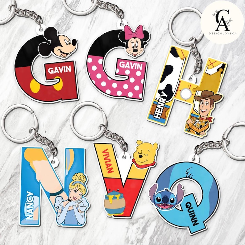May include: A collection of colorful character-themed keychains. The keychains feature the letters G, H, N, V, and Q, each with a different character design, including Mickey Mouse, Minnie Mouse, Woody, Cinderella, Winnie the Pooh, and Stitch. Each keychain has a name.