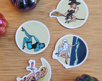 May include: Set of five round stickers featuring illustrations of women in various Halloween costumes. The stickers are printed on white paper with a glossy finish. The stickers feature a witch on a broomstick, a ghost, a woman in a blue dress, a woman in a red dress, and a woman in a waitress outfit.