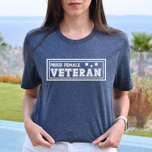 May include: A dark heather blue t-shirt features a white rectangular emblem with the text 'PROUD FEMALE VETERAN' and three white stars.  The shirt is a comfortable, casual style, suitable for everyday wear. This tee is perfect for showing pride and support for female veterans.
