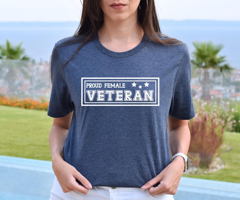May include: A dark heather blue t-shirt features a white rectangular emblem with the text 'PROUD FEMALE VETERAN' and three white stars.  The shirt is a comfortable, casual style, suitable for everyday wear. This tee is perfect for showing pride and support for female veterans.