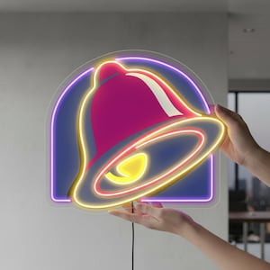 May include: A neon sign displaying the Taco Bell logo. The sign is shaped like a bell, with a pink centre, yellow highlights, and a purple border. The sign is held by two hands.