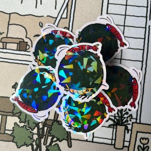 May include: A set of five iridescent holographic stickers featuring a black and green circle with a red shrimp on each sticker.