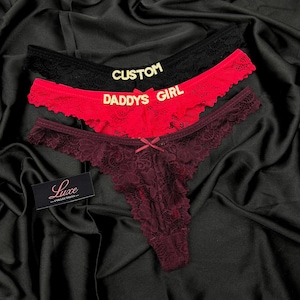 Pode incluir: Tr&ecirc;s tangas de renda nas cores preta, vermelha e bord&ocirc; escuro. O par preto apresenta o texto dourado CUSTOM, o par vermelho apresenta o texto dourado DADDYS GIRL e o par bord&ocirc; tem um pequeno la&ccedil;o. Uma etiqueta preta exibe Luxe COLLECTIONS.