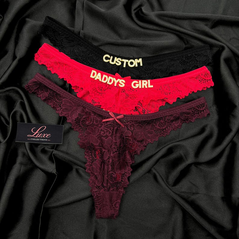 Pode incluir: Tr&ecirc;s tangas de renda nas cores preta, vermelha e bord&ocirc; escuro. A tanga preta apresenta o texto dourado CUSTOM, a vermelha o texto dourado DADDYS GIRL e a bord&ocirc; um pequeno la&ccedil;o central. Uma etiqueta preta exibe o texto Luxe COLLECTIONS.