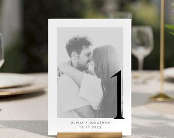 Puede incluir: Foto en blanco y negro de una pareja besándose, con el texto "Olivia + Jonathan 10.11.2025" y el número "1" en una fuente grande y en negrita. Esta es una tarjeta de número de mesa para una boda.