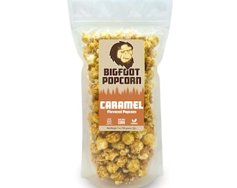 May include: A clear plastic bag filled with caramel flavored popcorn. The bag has a brown label with a cartoon Bigfoot and the text "Bigfoot Popcorn" and "Caramel Flavored Popcorn". The label also includes a non-GMO and vegan logo.