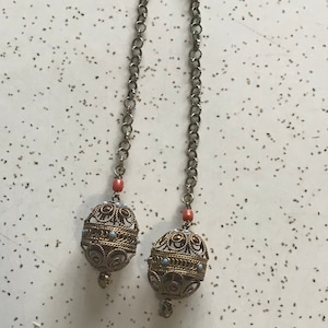 May include: A silver chain necklace with two gold filigree balls at the ends. The balls are decorated with small blue beads and have a coral-colored bead at the top.