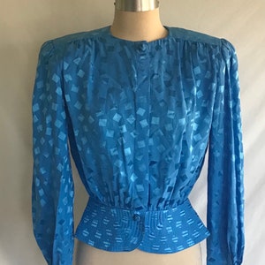 May include: A blue, long-sleeved blouse with a geometric pattern. The blouse has a fitted waist and a button-up front.