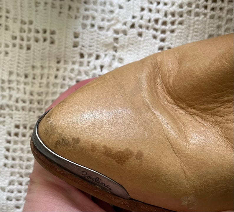 May include: Close-up of a tan leather boot with a silver metal trim and the word "Zodiac" embossed on the side.