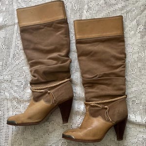 May include: A pair of brown suede knee-high boots with a braided detail around the ankle and a pointed toe.