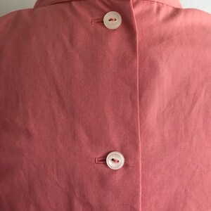 May include: The back of a dusty rose colored shirt with three white buttons.