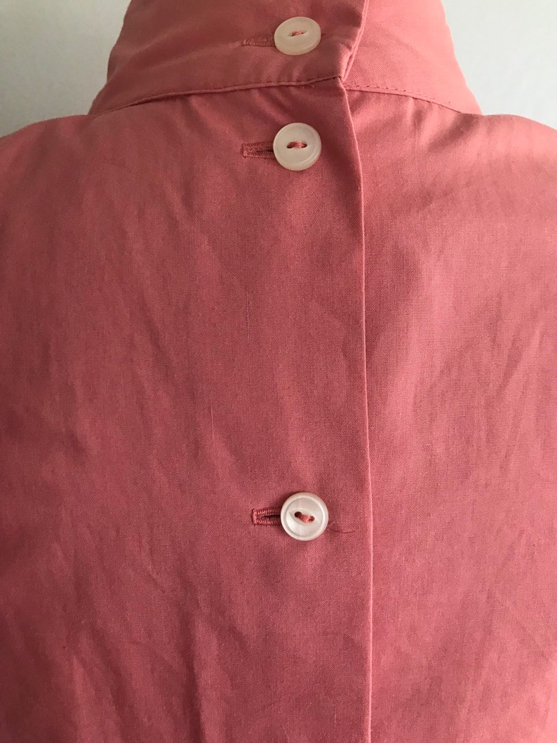 May include: The back of a dusty rose colored shirt with three white buttons.