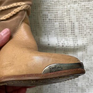 May include: Tan leather ankle boots with a silver metal plate on the heel that says "Zodiac" in cursive.