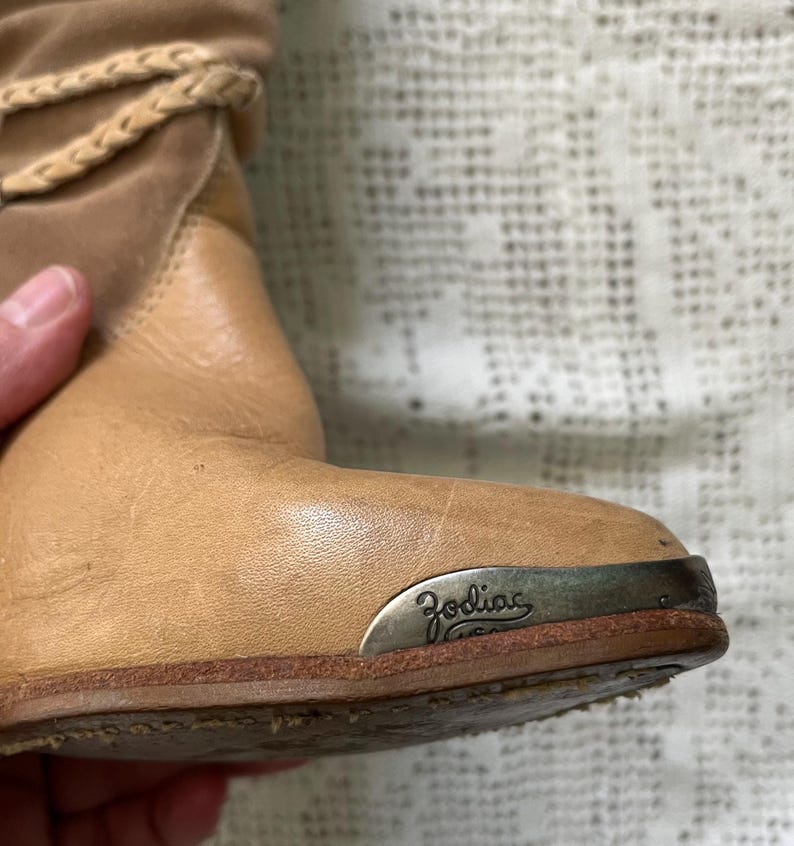 May include: Tan leather ankle boots with a silver metal plate on the heel that says "Zodiac" in cursive.
