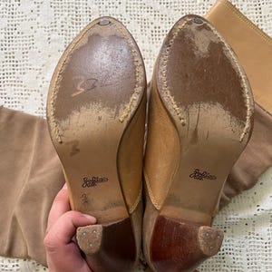 May include: A pair of brown suede knee-high boots with a wooden heel. The boots have a zipper on the inside of the leg and the brand name "Zodiac" is printed on the sole.