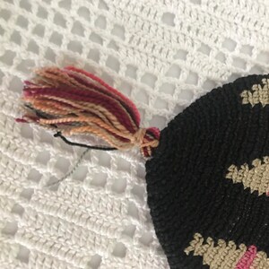 May include: A black crocheted bag with a pink and beige pattern and a multi-colored tassel.