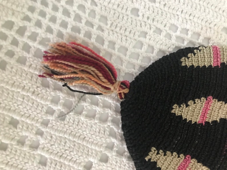 May include: A black crocheted bag with a pink and beige pattern and a multi-colored tassel.