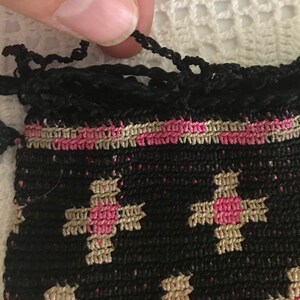 May include: A small black crocheted bag with a pink and beige pattern. The bag has a drawstring closure and a tassel.
