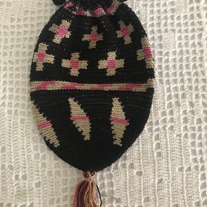 May include: A black crocheted drawstring bag with pink and beige geometric patterns. The bag has a tassel at the bottom.