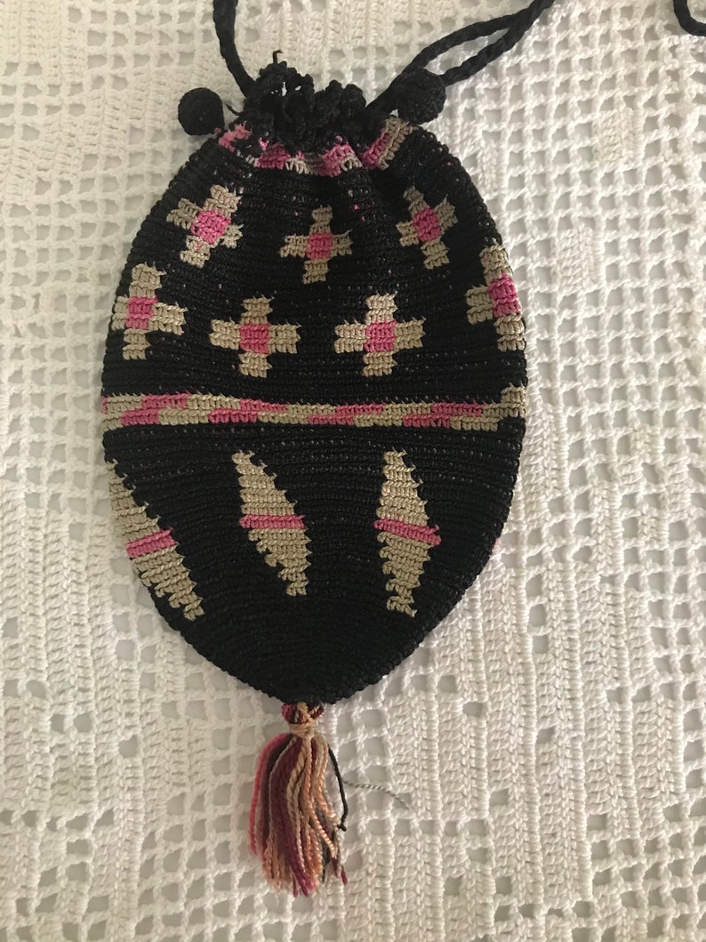 May include: A black crocheted drawstring bag with pink and beige geometric patterns. The bag has a tassel at the bottom.