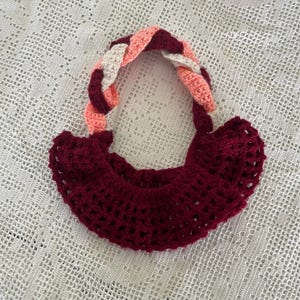 May include: A crocheted burgundy bag with a pink and white braided handle.