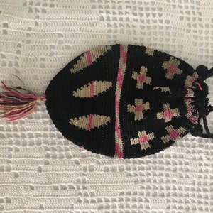May include: A black crocheted drawstring bag with pink and beige accents. The bag has a tassel and a long black drawstring.