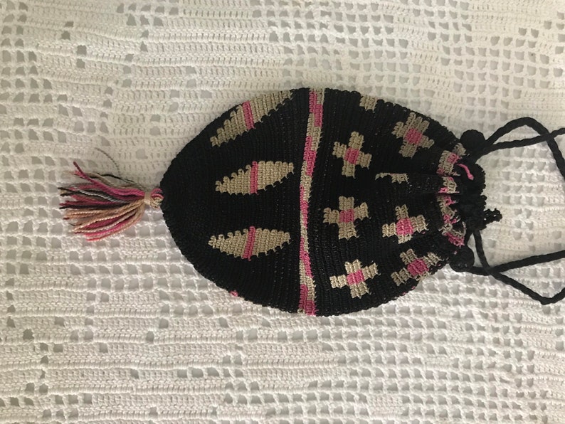 May include: A black crocheted drawstring bag with pink and beige accents. The bag has a tassel and a long black drawstring.