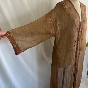 May include: A sheer, bronze-colored long-sleeve robe featuring intricate rust-colored embroidery along the front opening and sleeve cuffs. The garment is accented with small, round, dark-toned decorative beads along the edges and floral patterns.