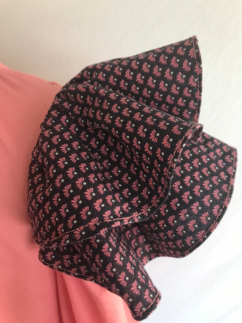 May include: A pink and black patterned fabric with a ruffled edge. The fabric is folded over itself, creating a layered effect.