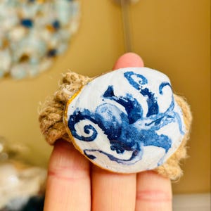 May include: A white ceramic mug with a black handle and the text "But First, Coffee" in a bold, black font. The mug is set against a blurred background, suggesting a cozy setting.